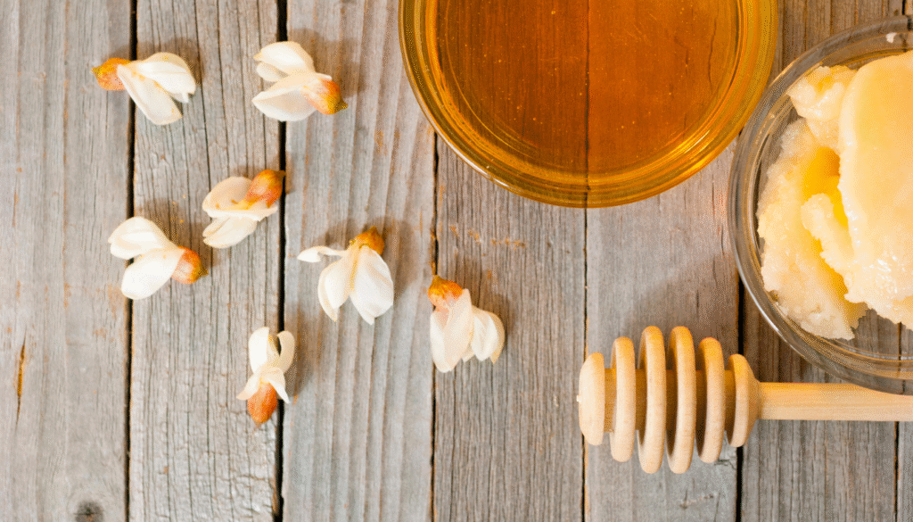 A close-up of a glass jar filled with golden acacia honey, its surface glistening with a warm, amber glow. The honey appears thick and viscous, with delicate bubbles rising to the surface. The jar is set against a blurred, neutral background, allowing the honey to be the central focus. Soft, diffused lighting illuminates the scene, creating a cozy and inviting atmosphere. The image conveys the natural sweetness and purity of this versatile acacia honey, ready to be savored and enjoyed. Miel D'acacia